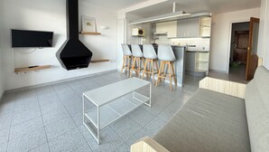 A modern living room with a TV, a black fireplace, a dining area with bar stools, and a kitchen with a large island. - Agi Pi Sunyer 4 1A Apartamento for rent in Roses Girona. (Roses)