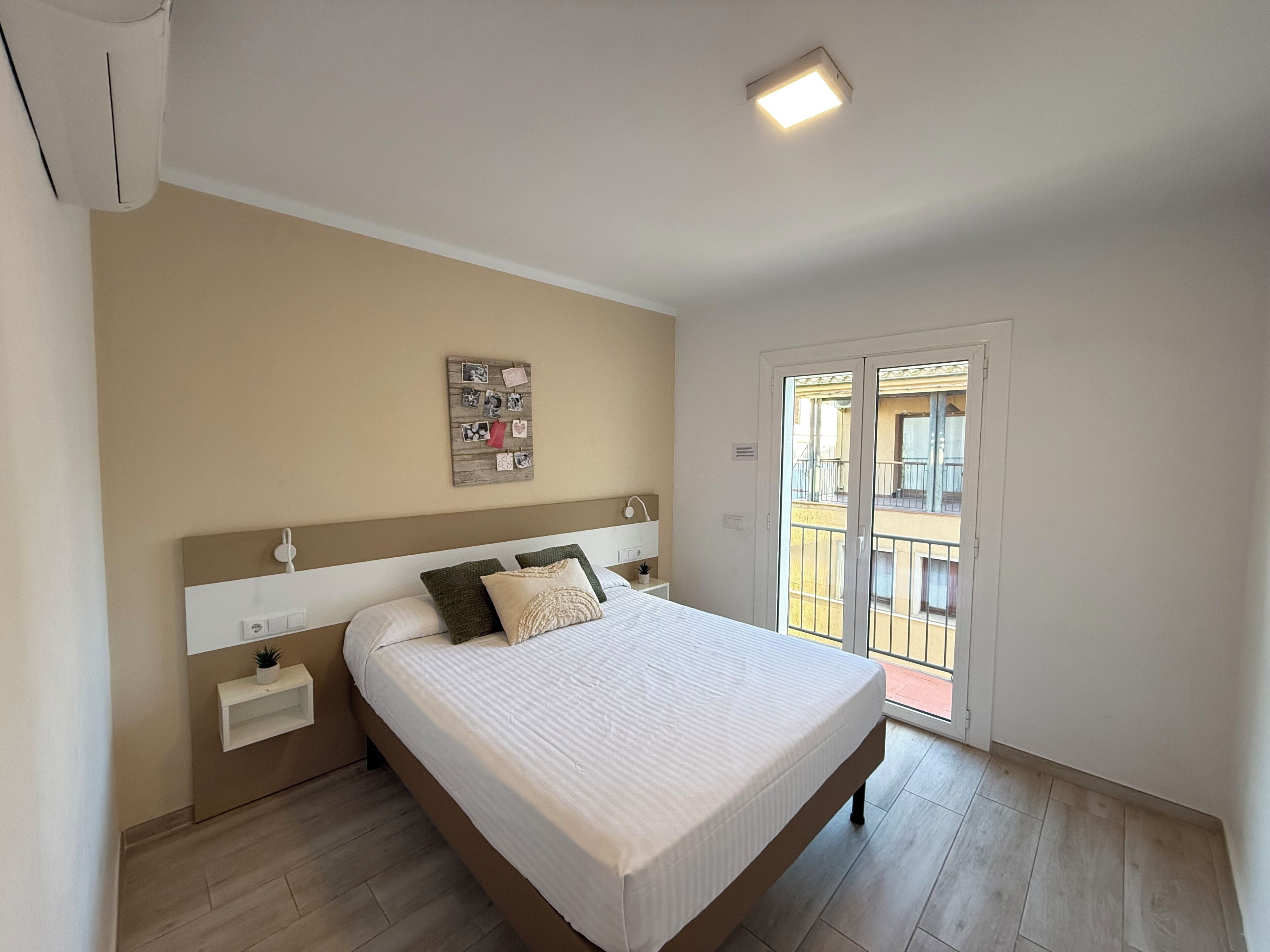 Un dormitorio con cama, mesita de noche, expositor de fotos en la pared y vistas al balcón exterior.