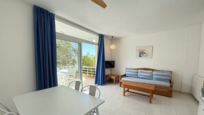 A room with a dining table, chairs, a sofa, a TV, and a ceiling fan. - Agi Rescator 117 Apartamento for rent in Roses Girona. (Rosas / Roses)