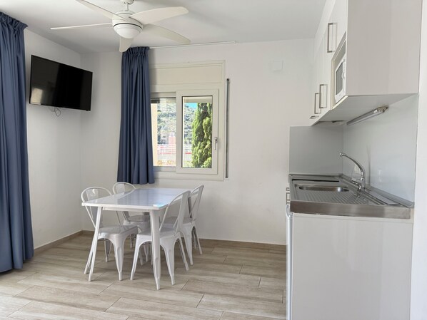 A small, modern kitchen with a dining table and chairs, a ceiling fan, a flat-screen TV, and a window with curtains. - Agi Rescator 229 Apartamento for rent in Roses Girona. (Roses)