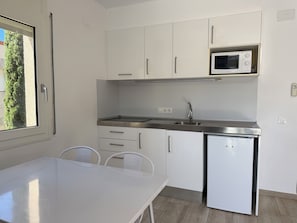 A compact kitchen with white cabinets, a microwave, a sink, and a small refrigerator.