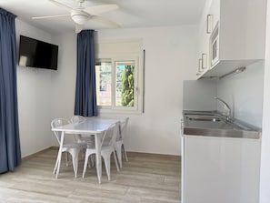 Une petite cuisine moderne avec une table et des chaises, un ventilateur de plafond, un téléviseur à écran plat et une fenêtre avec des rideaux.