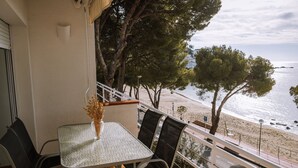 Un balcón con mesa y sillas, con vista a una playa con árboles y el mar.