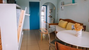 Una habitación con una cama, una mesa de comedor, una silla, un televisor y una puerta que da a otra habitación.