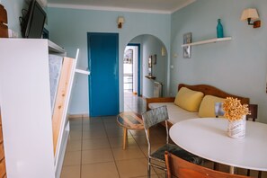 Een kamer met een bed, een ronde tafel, een stoel, een televisie en een deur naar een andere kamer.