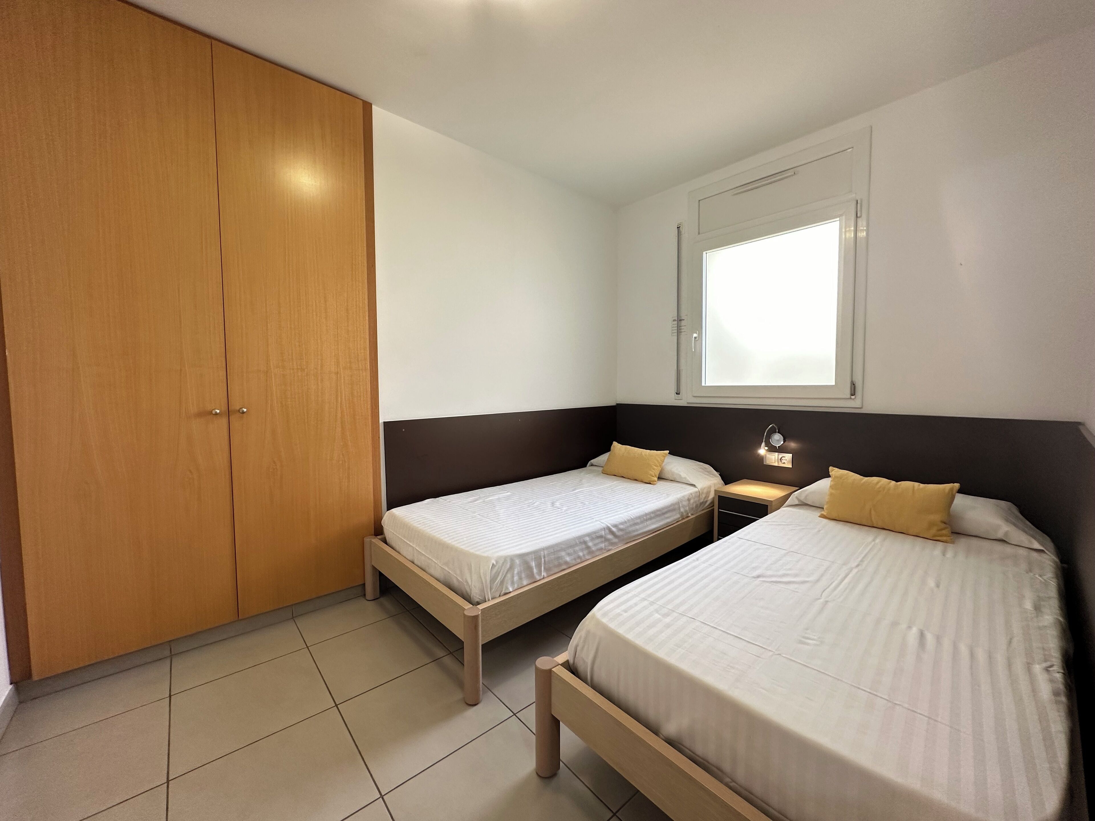 A bedroom with two single beds, a wardrobe, a nightstand, and a window.