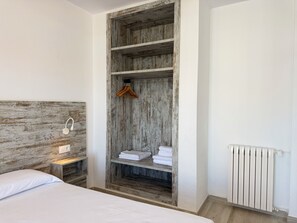 A bedroom with a wooden wardrobe, a bedside table with a lamp, and a radiator.