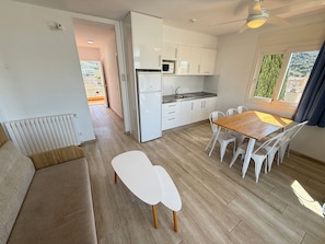 A modern kitchen with white cabinets, a dining area with a wooden table and white chairs, and a view of greenery outside.