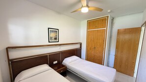 Un dormitorio con dos camas individuales, un armario de madera, un ventilador de techo y un cuadro en la pared.