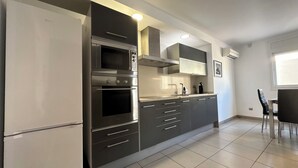 Une cuisine moderne dotée d’appareils électroménagers en acier inoxydable, de meubles de rangement gris et d’un sol carrelé.