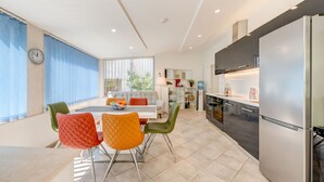 A modern kitchen with a built-in refrigerator, a dining area with colorful chairs, and a large window with blinds. - Luxury apartment positioned in a green oasis in the middle of the city (Split)