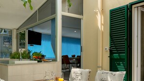 A dining area with a table set for two, a chair with a cushion, and a window with a view of the city. - Luxury apartment positioned in a green oasis in the middle of the city (Split)