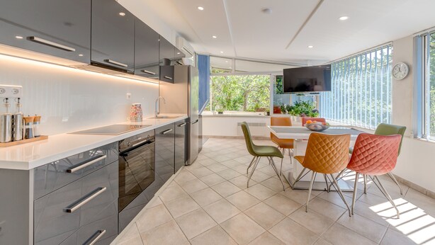 A modern kitchen with a dining area, featuring a large window, a flat-screen TV, and a dining table with chairs. - Luxury apartment positioned in a green oasis in the middle of the city (Split)