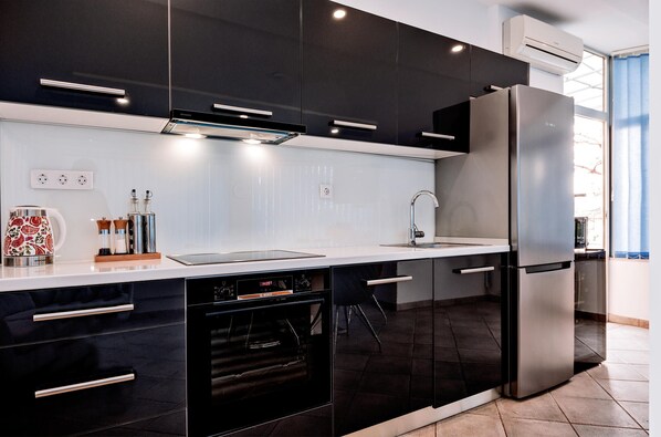 Une cuisine moderne avec des meubles noirs, des appareils en acier inoxydable et un plan de travail blanc.