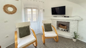 A living room with two wooden chairs, a television, a fireplace, and a checkered floor. - Agi Torre Quimeta Torre Apartamento for rent in Roses Girona. (Rosas / Roses)