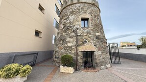 A stone tower with a small window and a door, surrounded by a paved area with potted plants. - Agi Torre Quimeta Torre Apartamento for rent in Roses Girona. (Rosas / Roses)