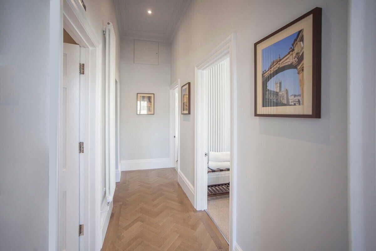 A hallway with white walls, a herringbone floor, and framed pictures on the walls.
