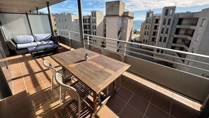 Un balcon avec une table et des chaises en bois, un canapé avec des coussins et une vue sur les bâtiments environnants.