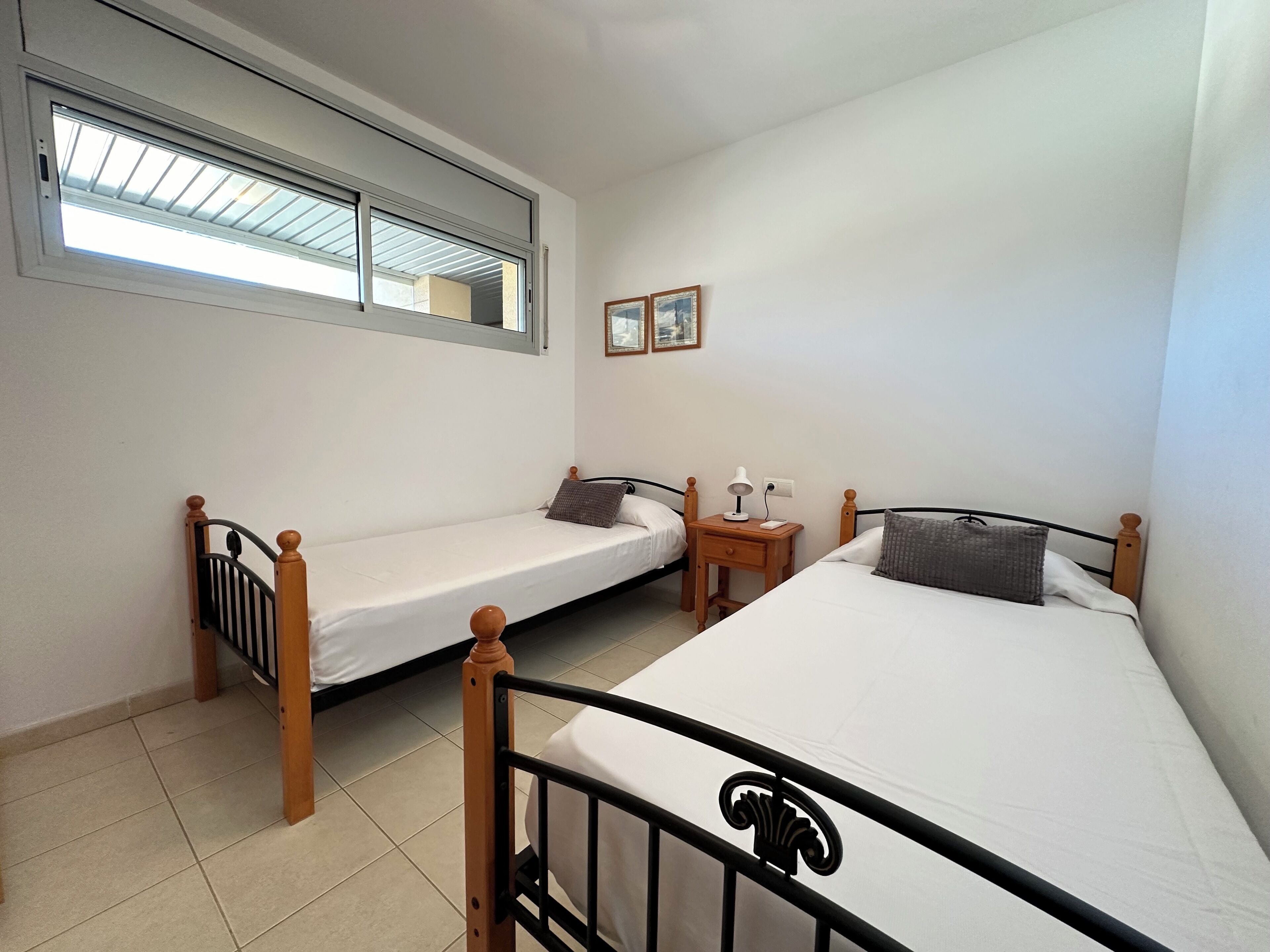 Una habitación con dos camas individuales, una mesita de noche con lámpara y una ventana con persianas.