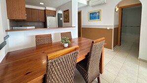 Une cuisine moderne avec des meubles en bois, un réfrigérateur encastré et un coin repas comprenant une table en bois et des chaises en osier.
