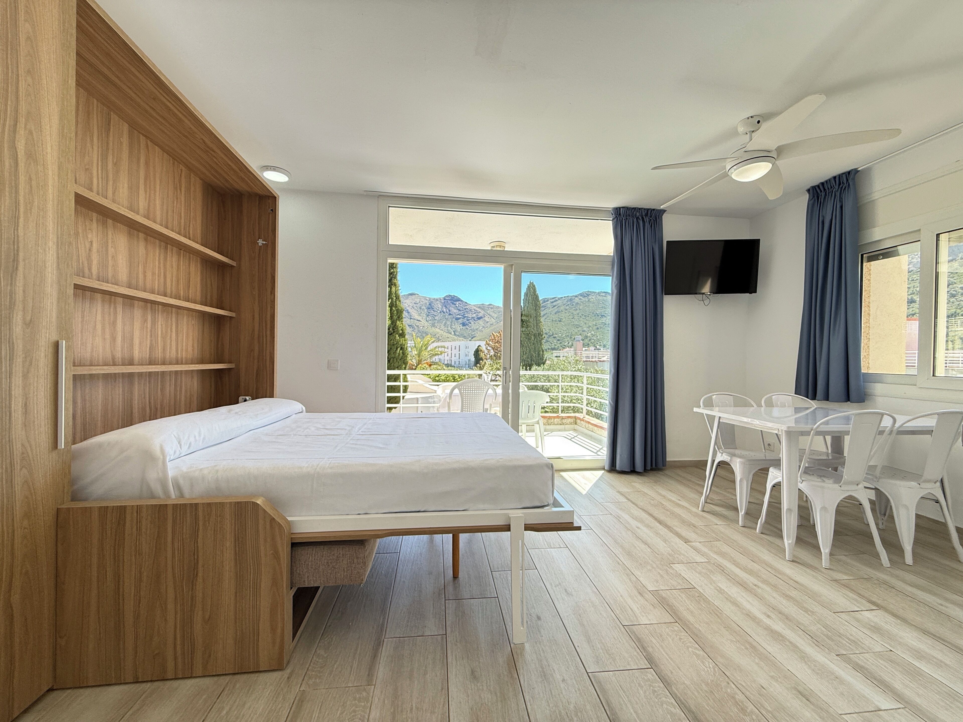 Ein Schlafzimmer mit einem Bett, einem Holzschrank, einem Balkon mit Stühlen und einem Fernseher.
