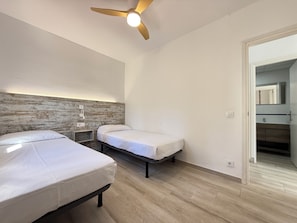 Une chambre avec deux lits, un ventilateur de plafond, une tête de lit en bois et une vue sur la salle de bain.