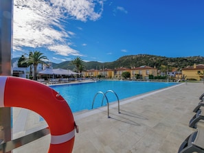 Piscina com boia salva-vidas, cadeiras de descanso e montanhas ao fundo.