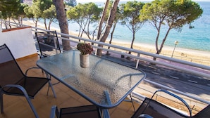 Ein Tisch mit Glasplatte und Stühlen auf einem Balkon mit Blick auf einen Strand.