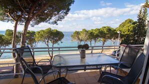 Eine Terrasse mit Glastisch und Stühlen mit Blick auf einen Strand und das Meer.