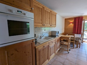 Eine Küche mit Holzschränken, einem eingebauten Backofen, einer Mikrowelle und einem Spülbecken.