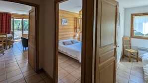 Ein Zimmer mit einem Bett, einem Sessel und einem Tisch. Ein Fenster bietet Blick auf Bäume.