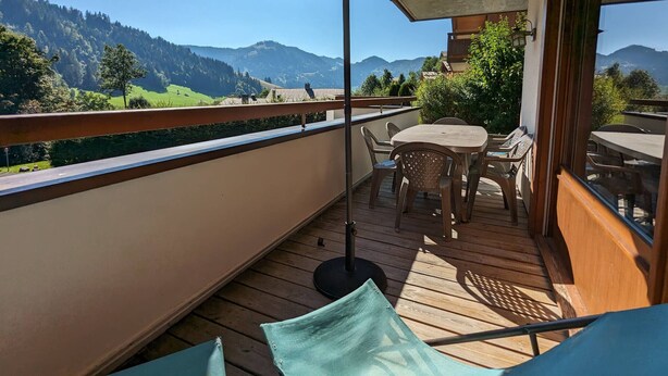 Eine Holzterrasse mit Tisch, Stühlen und Sonnenschirm, mit Blick auf die Berge.
