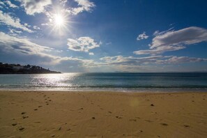 Ein Strand mit Fußspuren, die zum Wasser führen, ein klarer Himmel und strahlender Sonnenschein.