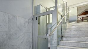 Un interno moderno con pavimento in marmo, porta dell'ascensore in vetro e scala in metallo.