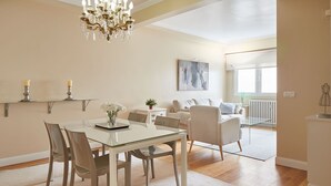 Un soggiorno moderno con un tavolo da pranzo in vetro, sedie, un divano e un lampadario.