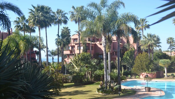 A resort with a swimming pool surrounded by palm trees and a building with balconies. - URBANIZATION ALICATE PLAYA. (Marbella)