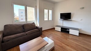 Un salon comprenant un canapé, une table basse, un téléviseur posé sur un meuble et une porte coulissante.