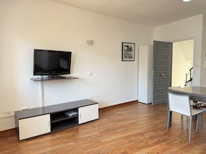 A modern living room with a flat-screen TV, a built-in cabinet, a dining table with chairs, and a door leading to another room. - Agi Josep Sabate 41 Apartamento for rent in Roses Girona. (Rosas / Roses)