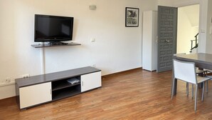 Un salon moderne doté d’un téléviseur à écran plat, d’une bibliothèque intégrée, d’une table à manger avec des chaises et d’une porte donnant sur une autre pièce.