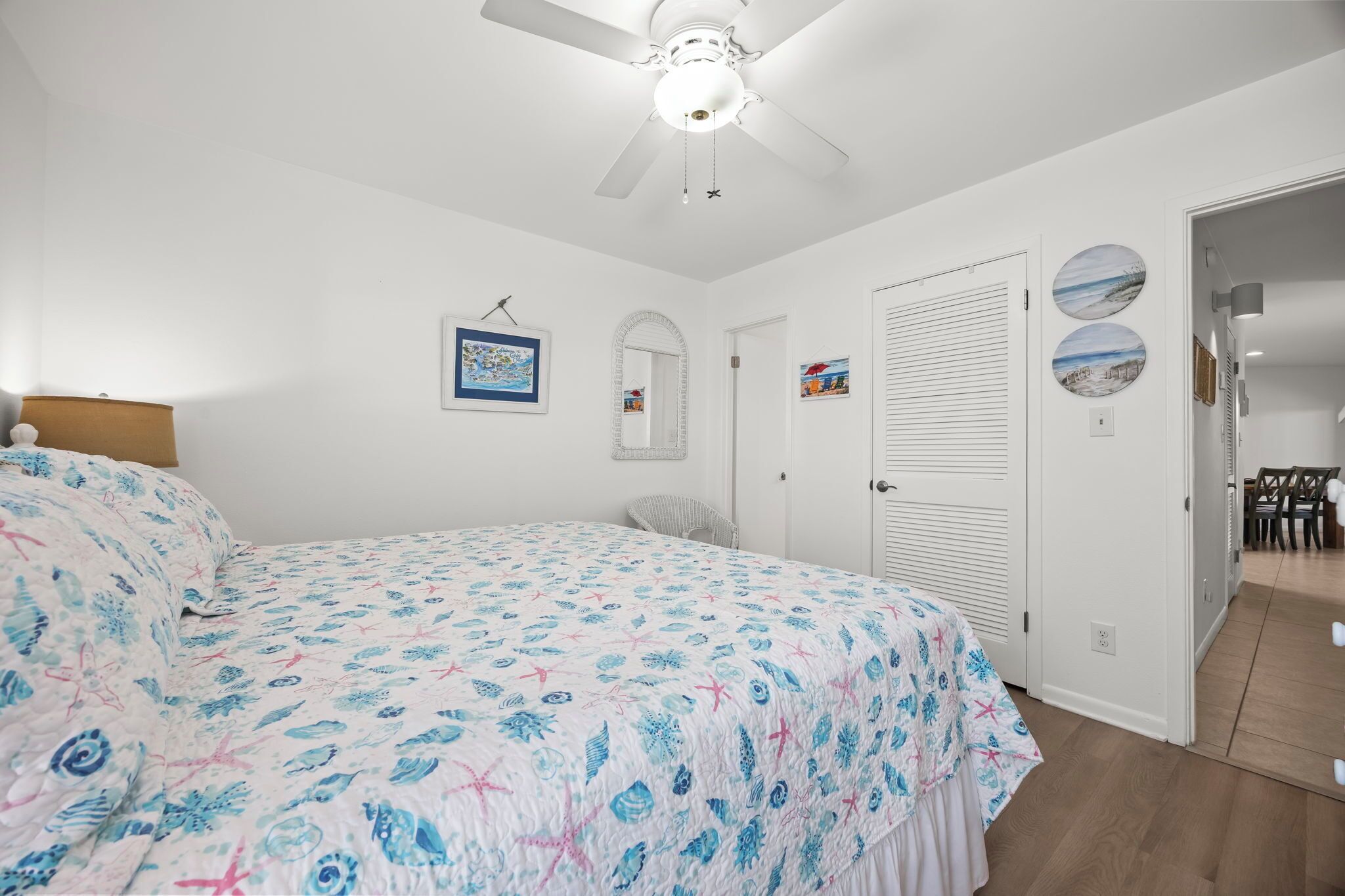 A bedroom with a bed, a ceiling fan, a door, and a wall with two pictures.