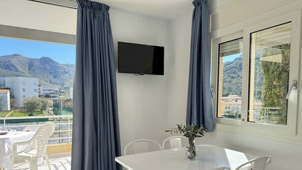 Quarto com uma mesa de jantar, cadeiras, televisão e janela com cortinas.
