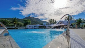 Uma piscina com água azul cristalina, rodeada por um deck ladrilhado e palmeiras.