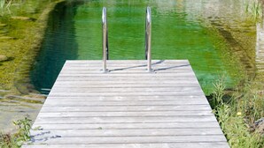 Une jetée en bois qui mène à un étang, avec un petit kiosque et des chaises longues en arrière-plan.