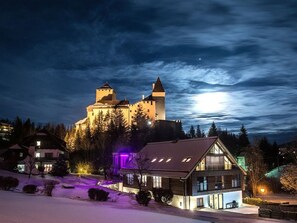 Ein schlösserähnliches Gebäude mit einem Turm, umgeben von Bäumen und Schnee.