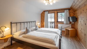 Une chambre avec un plafond en bois, un lit recouvert de draps blancs, une table de chevet avec une lampe et un téléviseur fixé au mur.