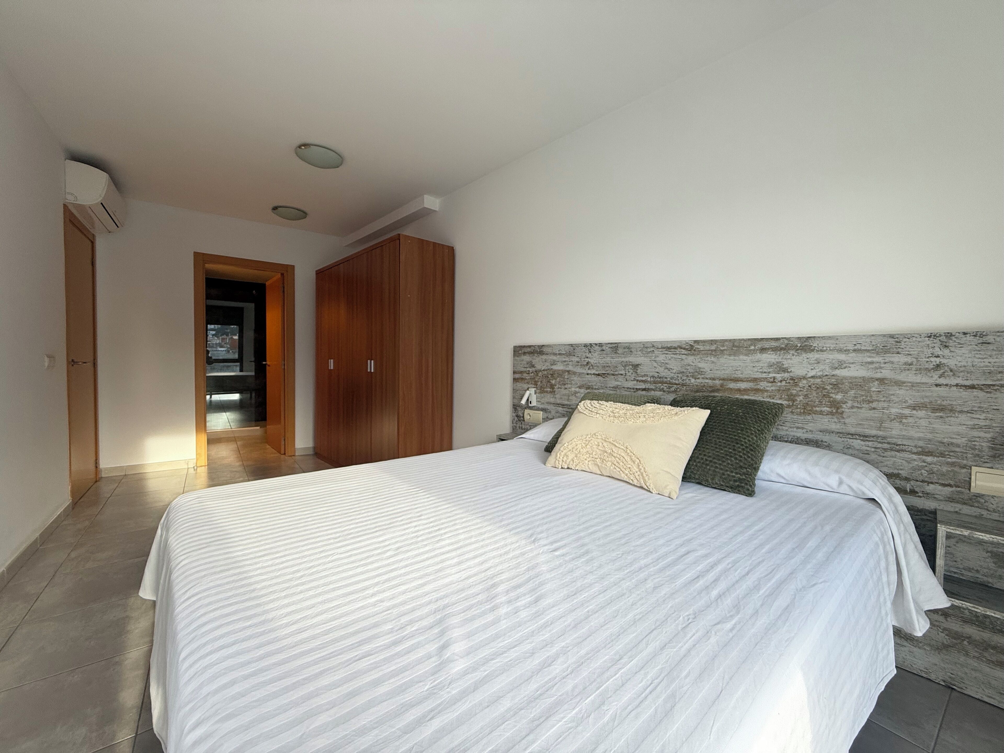 Quarto com cama grande, guarda-roupa de madeira e vista da cidade por uma porta aberta.