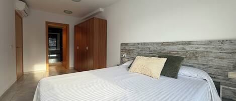 Quarto com cama grande, guarda-roupa de madeira e vista da cidade por uma porta aberta.