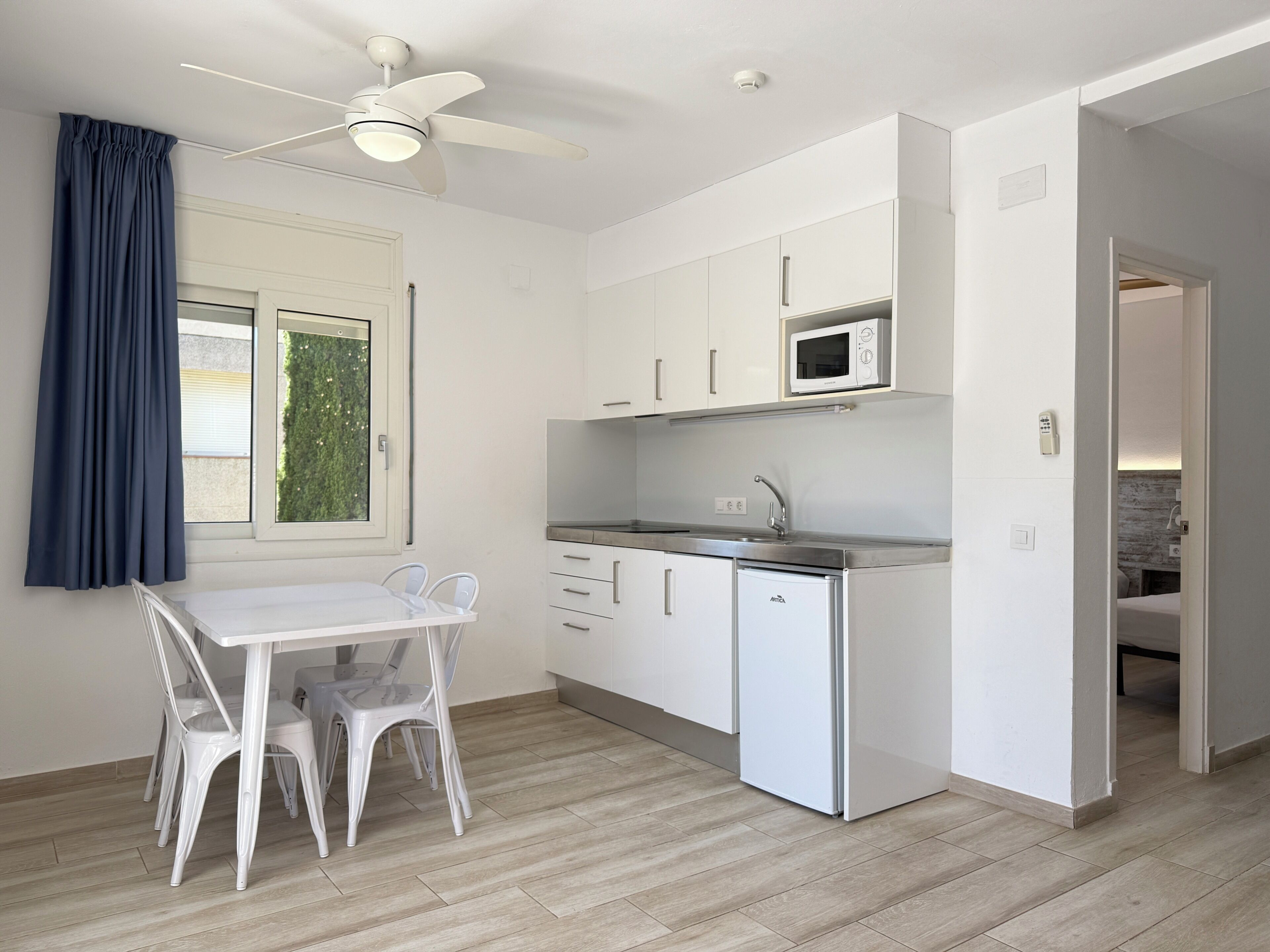 A compact kitchen with white cabinets, a microwave, a sink, and a ceiling fan.