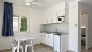 Een compacte keuken met witte kasten, een magnetron, een spoelbak en een plafondventilator.