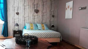 Un dormitorio con pared de madera, una cama con ropa de cama estampada, una mesita de noche con lámpara y un radiador.
